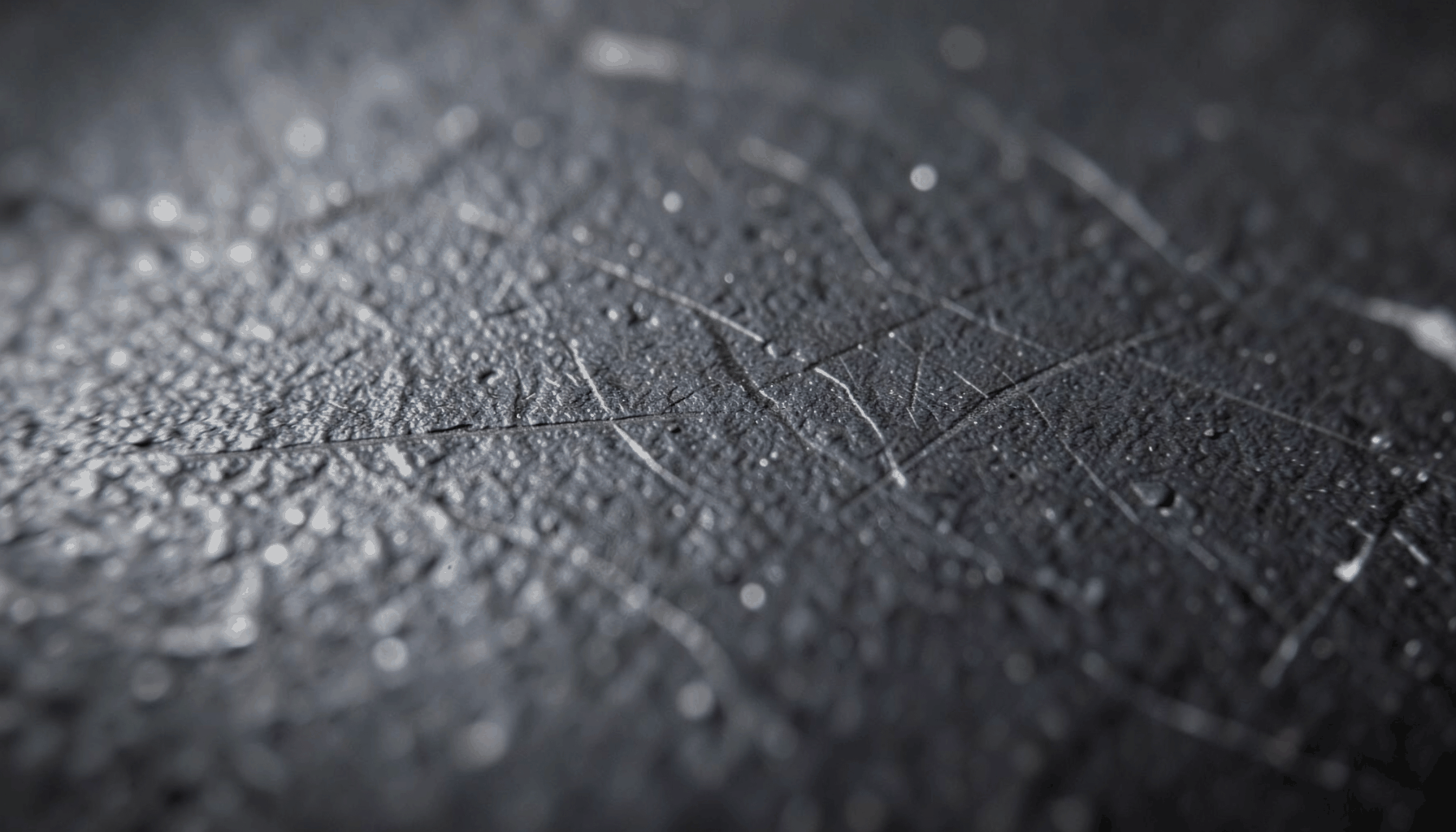Close-up of textured dark metal with faint scratches, moody and industrial.