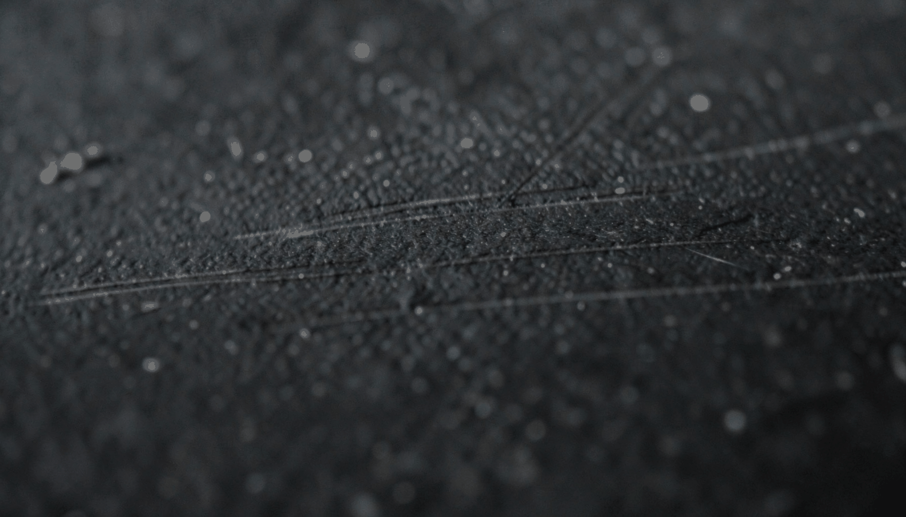 Close-up of dark textured metal with faint horizontal scratches, moody and industrial.